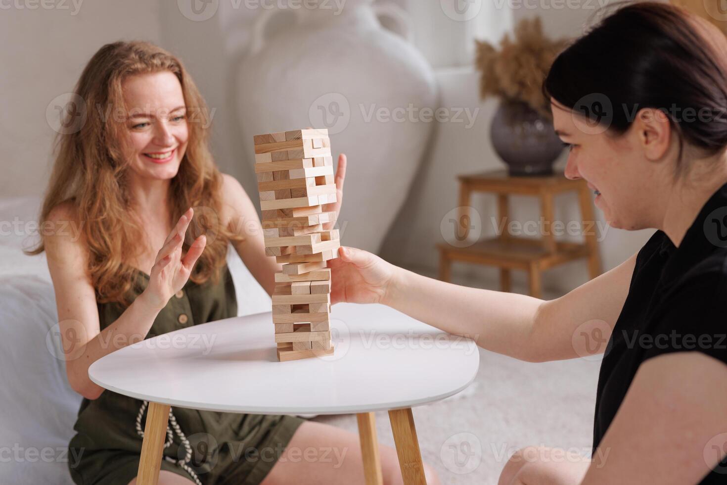 two women playing a board game made of wooden blocks at home, excitement and relaxation, mind development concept, hand motor skills, photo