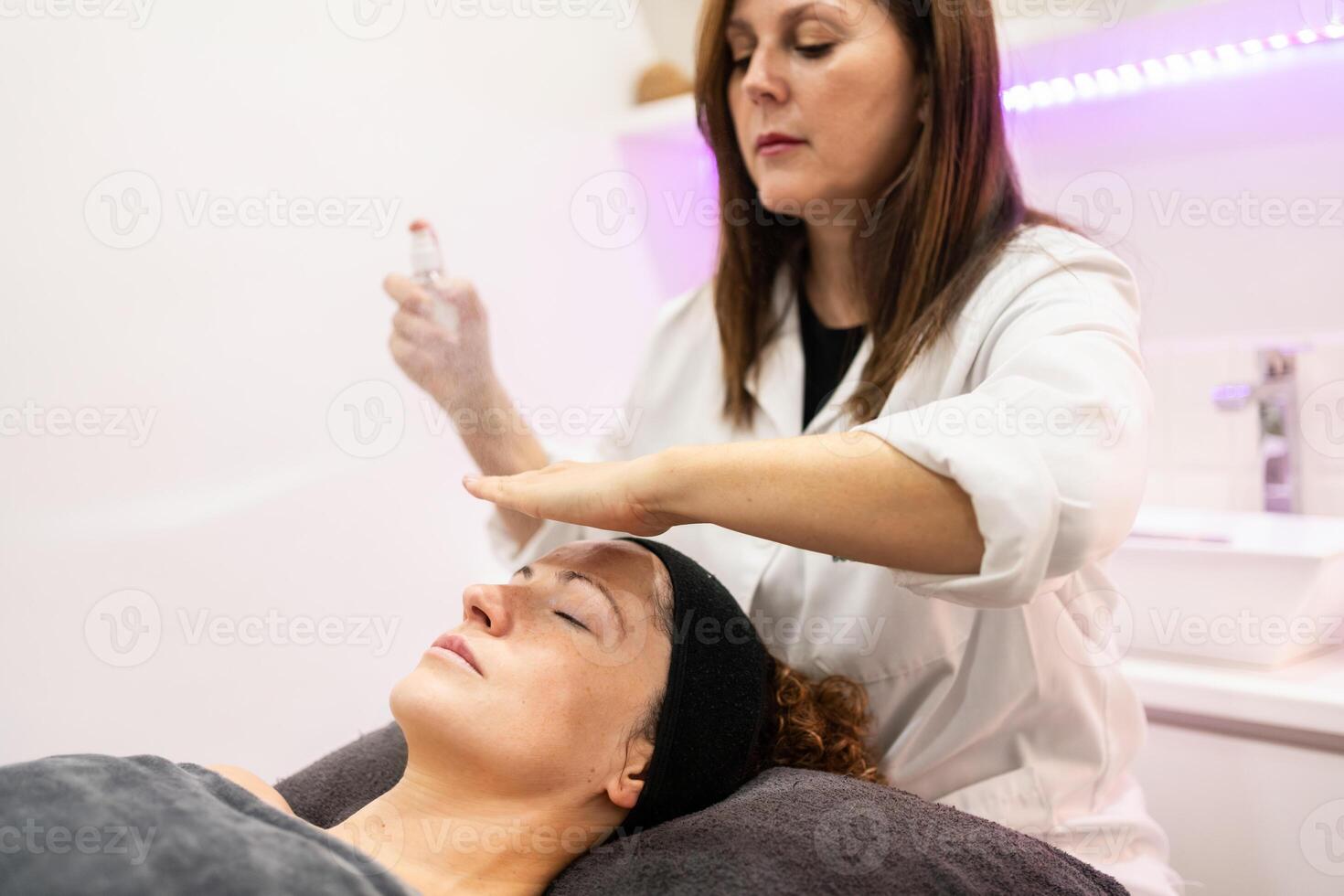 Concentrated woman applying cosmetic product on client face photo