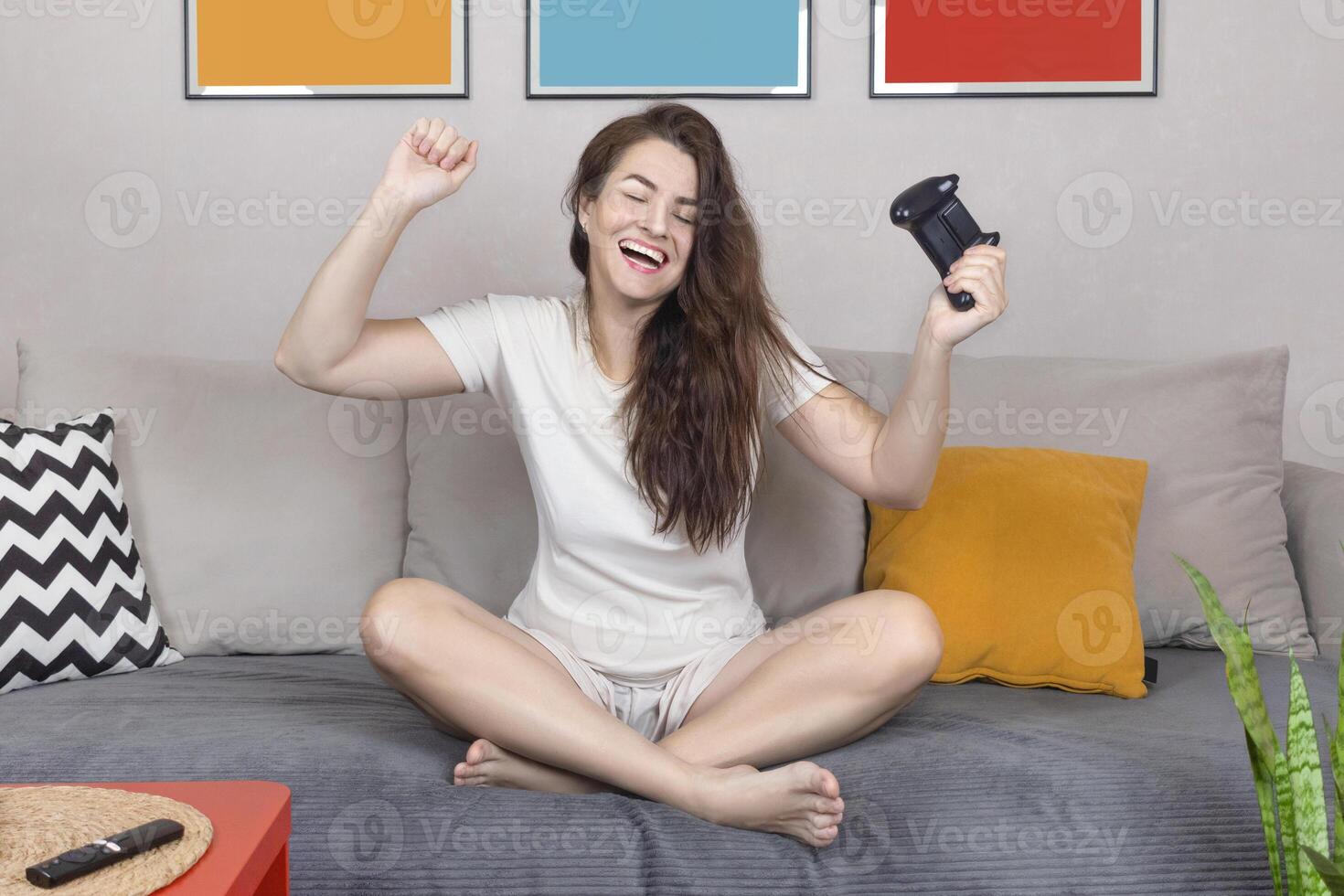 Brunet woman rejoices in the victory in the online game on the console. She is smile, sit relax on sofa at home have fun play online game. Close up photo