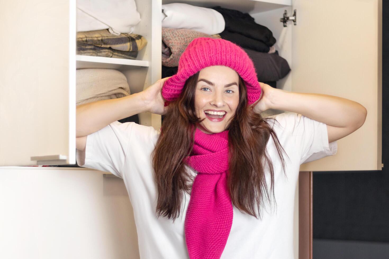 Woman smiles, she found her favorite knitted pink hat and scarf in the closet. Tries on himself, waiting for autumn, winter to wear warm clothes, close up photo