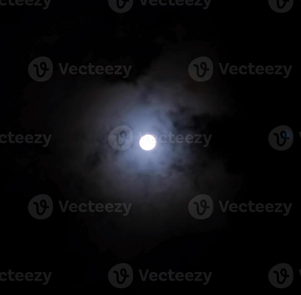 Close up detail of the full moon shining through the bluish clouds photo