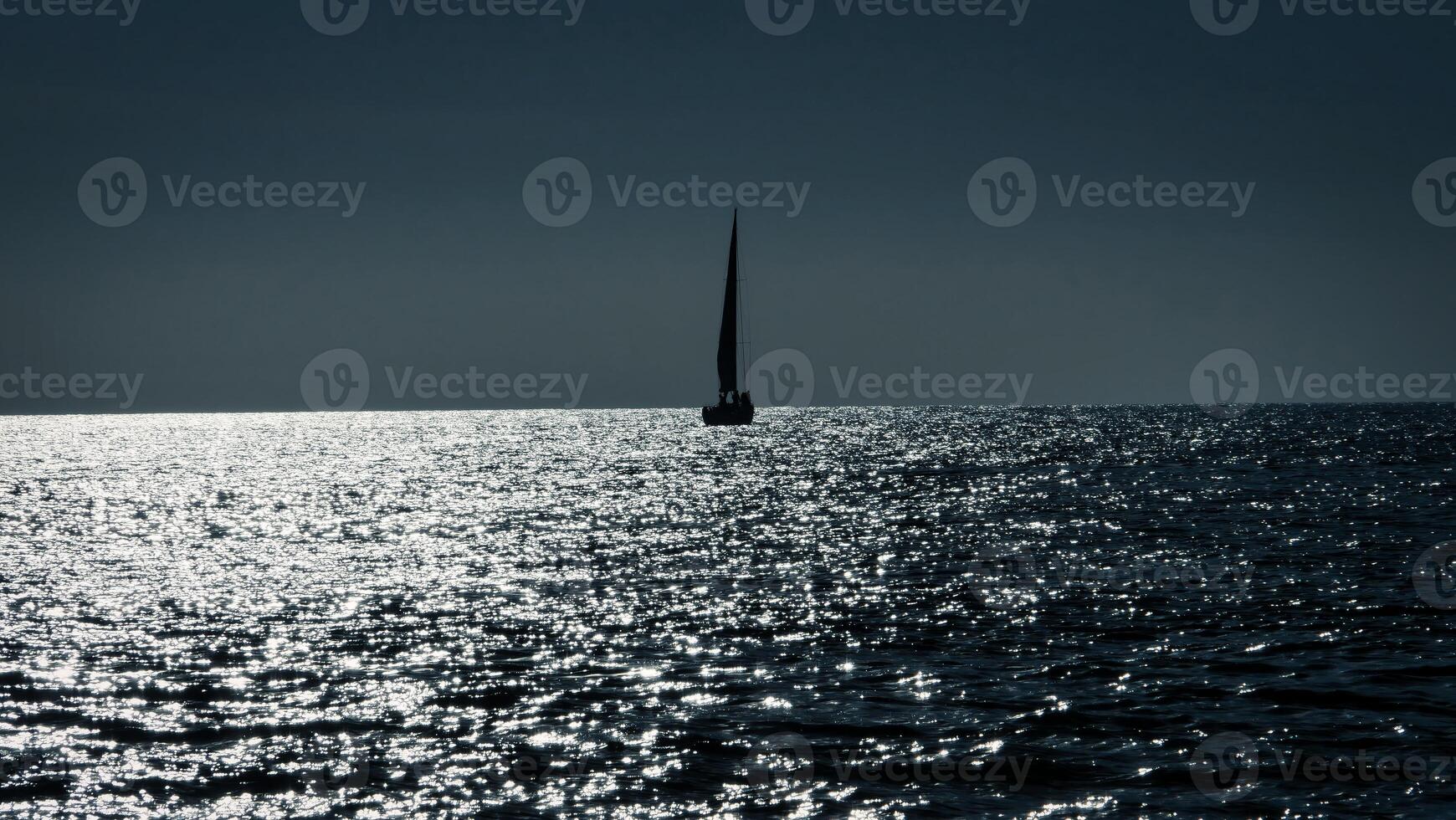 Lonely sailboat sailing on calm ocean under dark sky photo