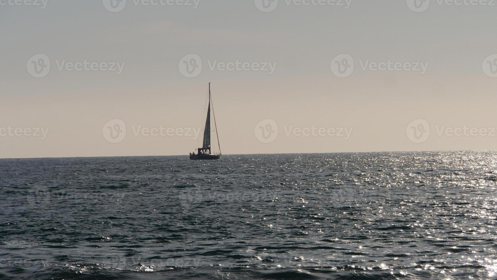 Sailboat sailing away on calm ocean at sunset with sun reflecting on water photo