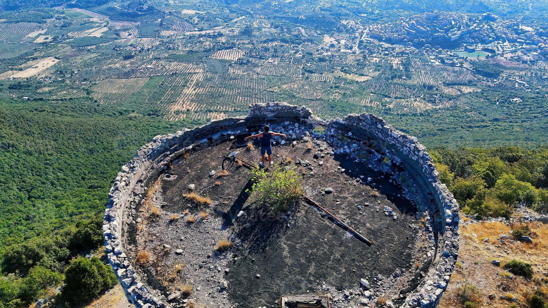 Young man standing with open arms on top of an old ruined building enjoying the view of the valley photo