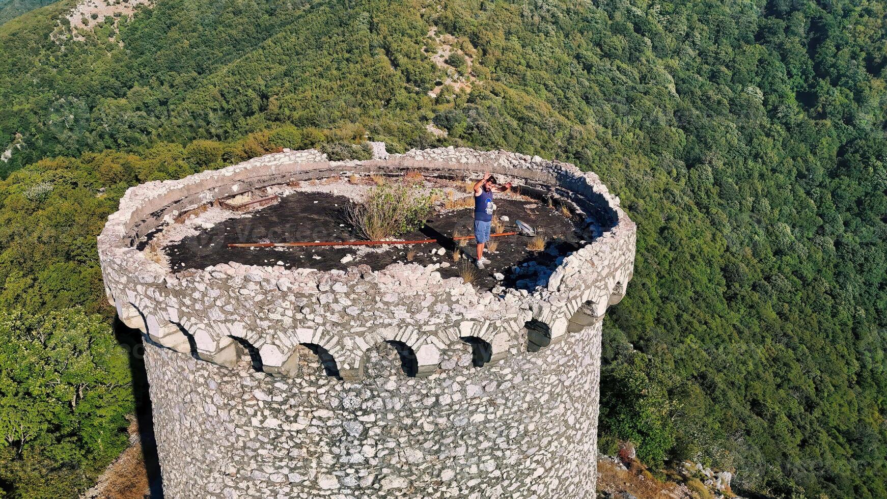Man celebrating on top of an old ruined stone tower with forest below photo