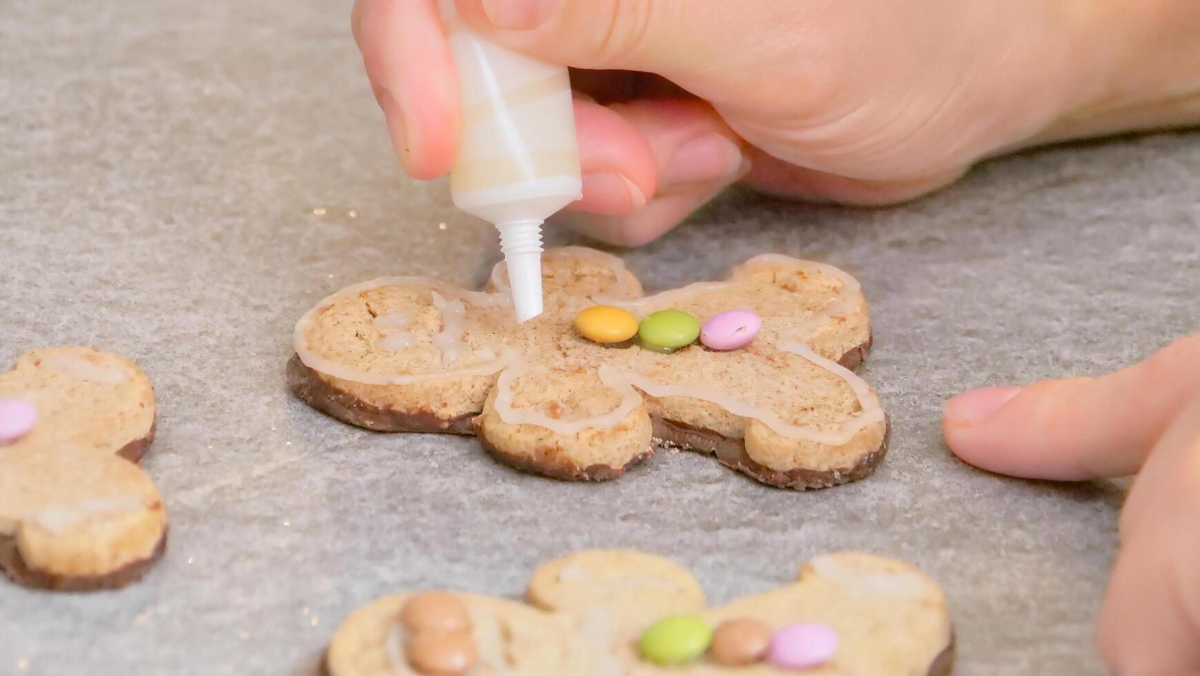 woman's hands decorating a gingerbread man-shaped Christmas cake with white icing and colored caramels, close-up photo