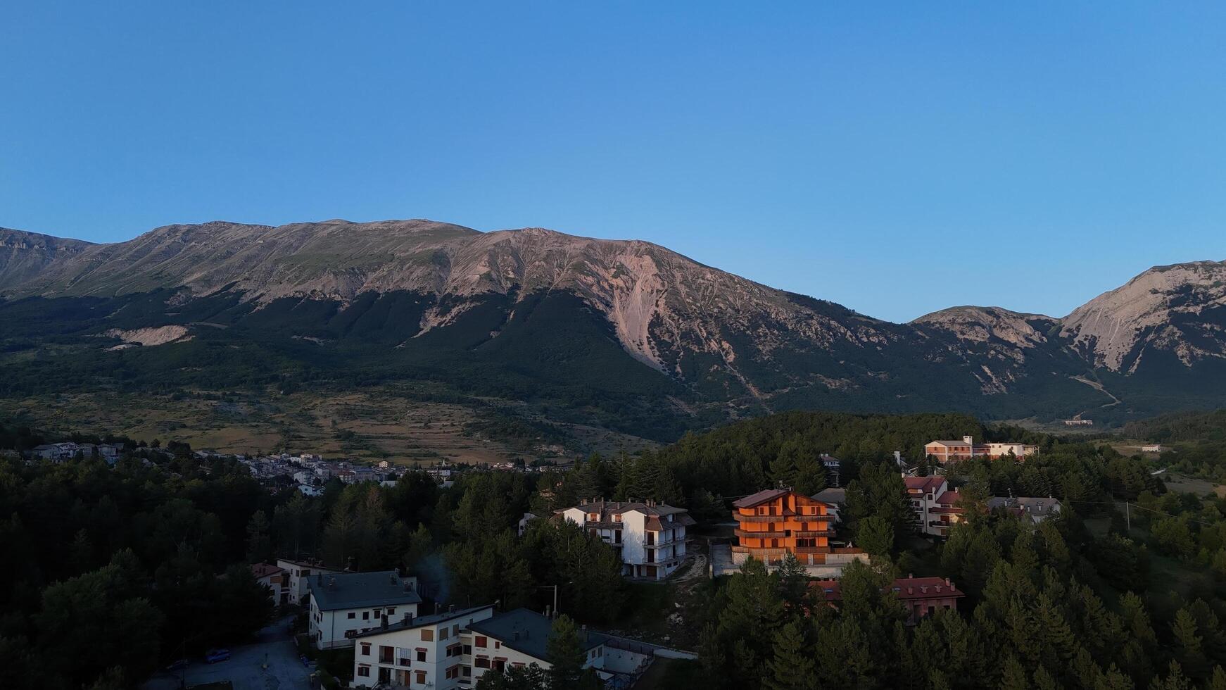 Golden hues of dusk illuminate a serene hillside village nestled beneath majestic mountains in tranquil evening light photo
