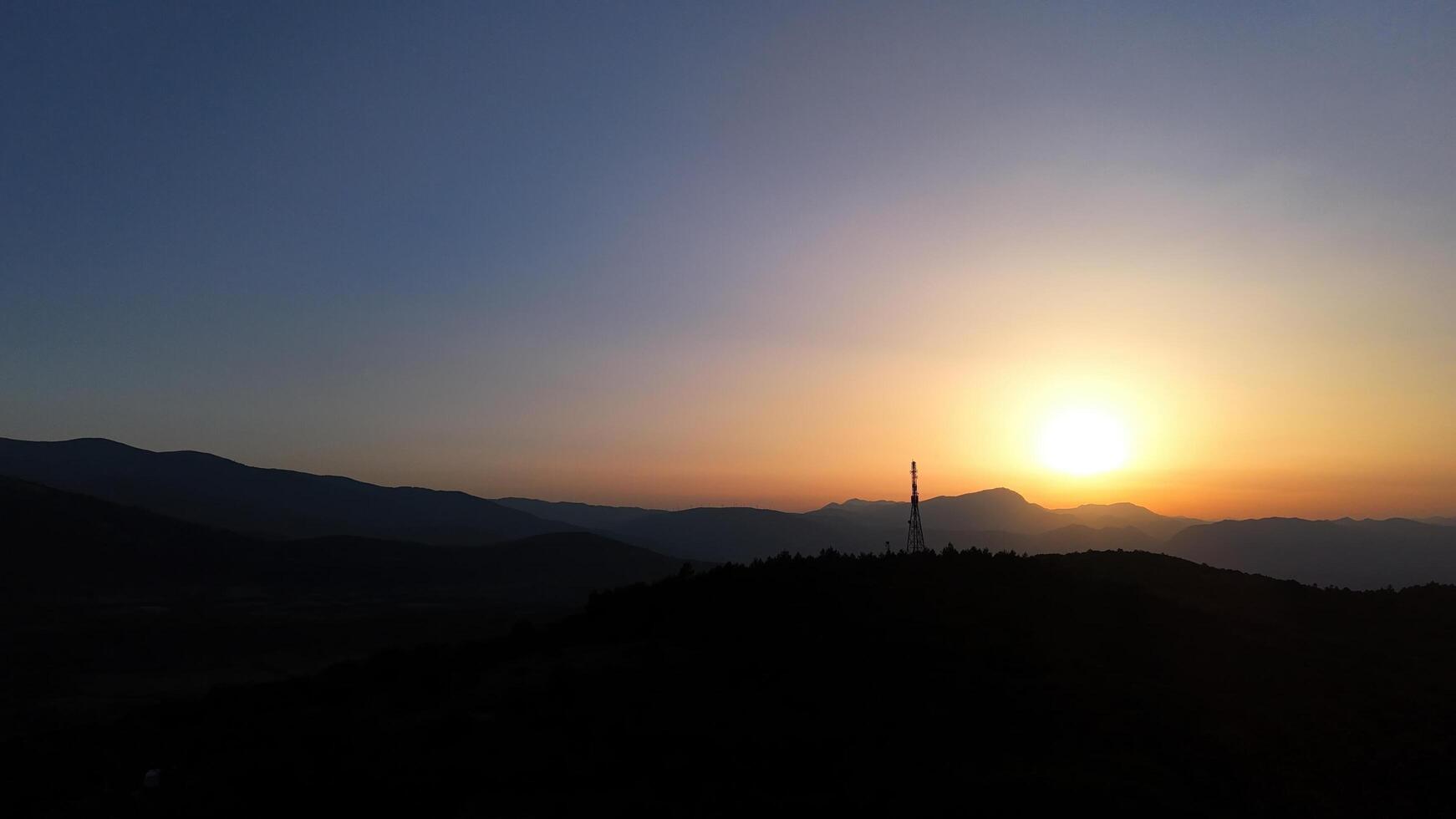 Serene sunrise over distant mountains paints the sky in hues of orange and blue, welcoming a new day on the horizon photo