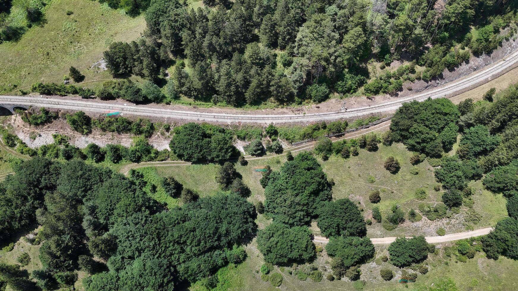 Aerial view of a winding railway nestled among vibrant green forests in the serene countryside during a sunny afternoon photo