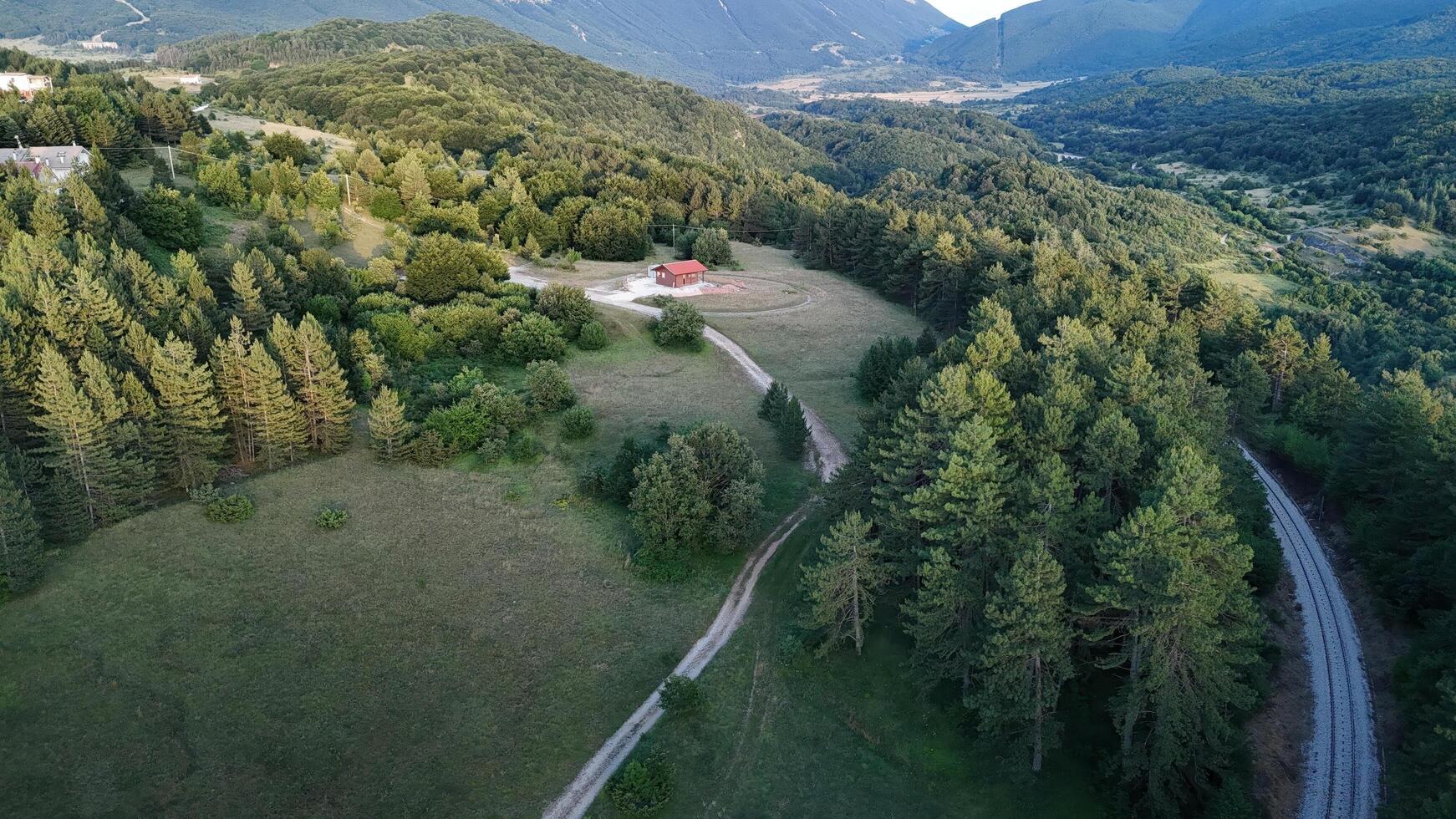 Aerial view of a serene green landscape with a small red cabin nestled among trees in the mountains during daylight photo