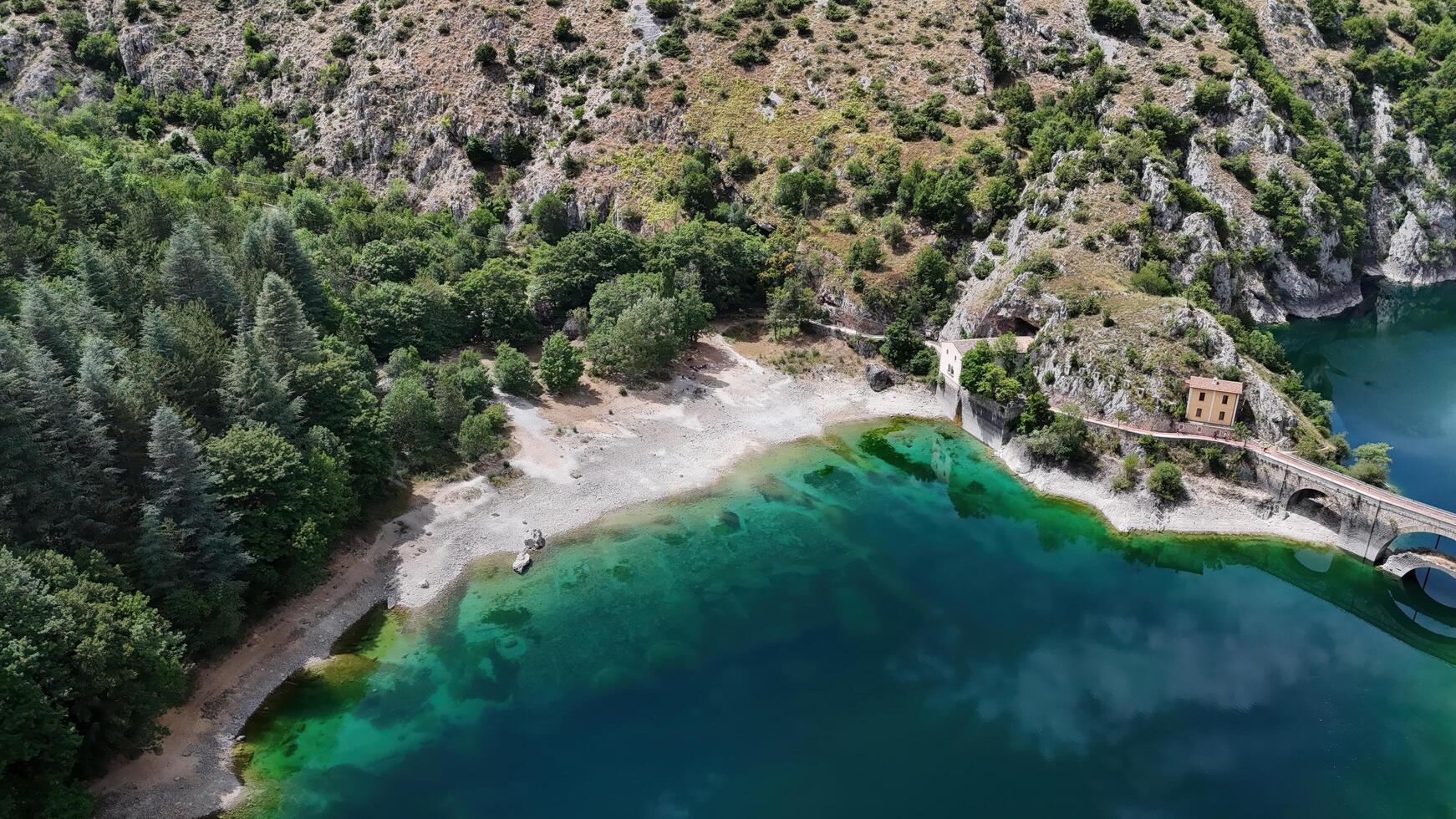 Serene shoreline embraced by lush greenery and rocky cliffs at a tranquil lake during a bright sunny day in early summer photo