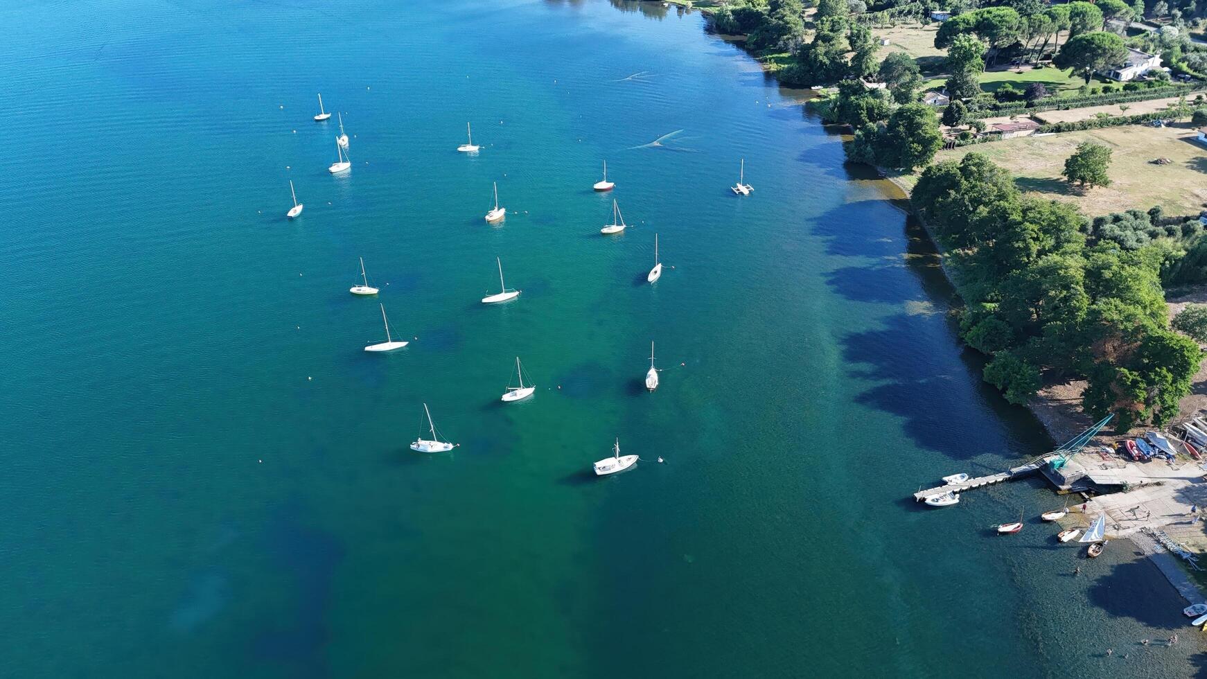Sailboats gently anchored in tranquil waters by a lush green shoreline under a clear blue sky during a serene summer afternoon photo