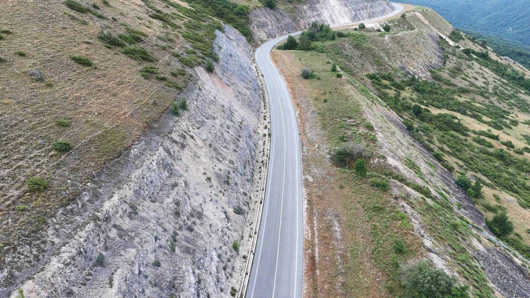 Winding mountain road surrounded by rugged terrain in a serene landscape during the afternoon sunlight photo