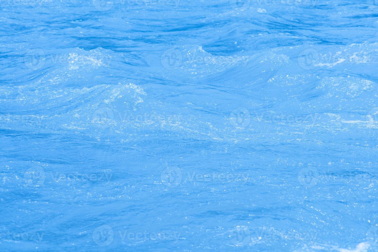 Bluewater waves on the surface ripples blurred. Defocus blurred transparent blue colored clear calm water surface texture with splash and bubbles. Water waves with shining pattern texture background. photo