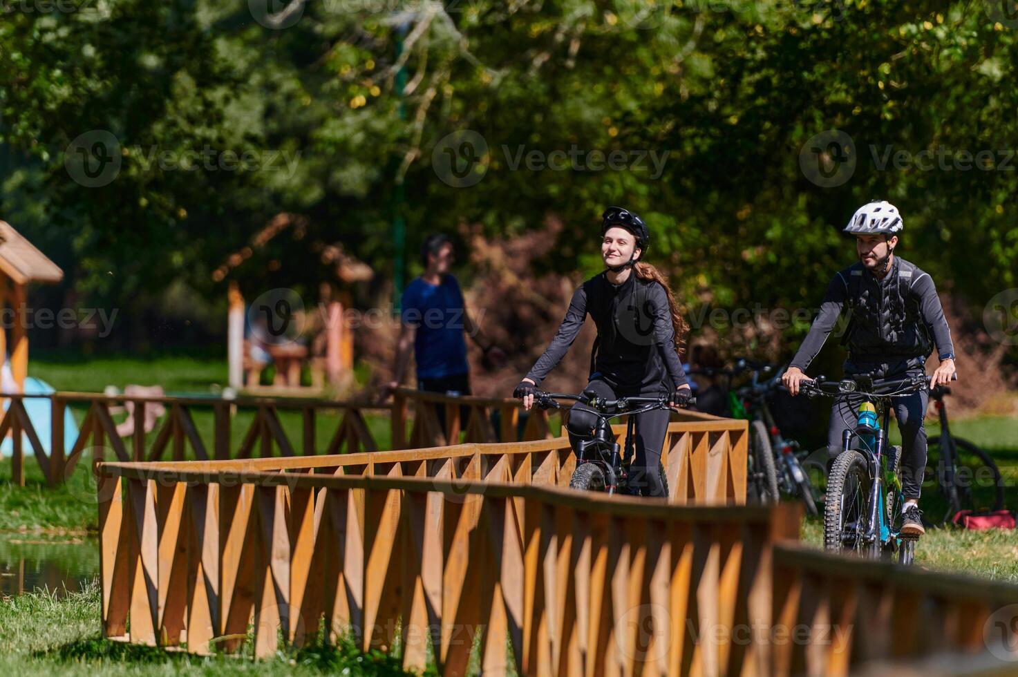 A blissful couple, adorned in professional cycling gear, enjoys a romantic bicycle ride through a park, surrounded by modern natural attractions, radiating love and happiness photo