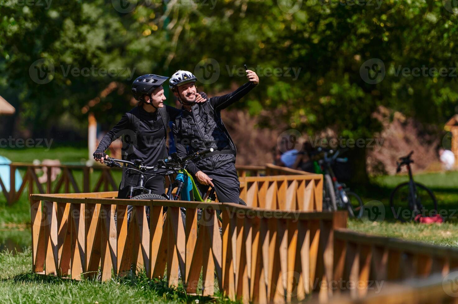 A blissful couple, adorned in professional cycling gear, enjoys a romantic bicycle ride through a park, surrounded by modern natural attractions, radiating love and happiness photo