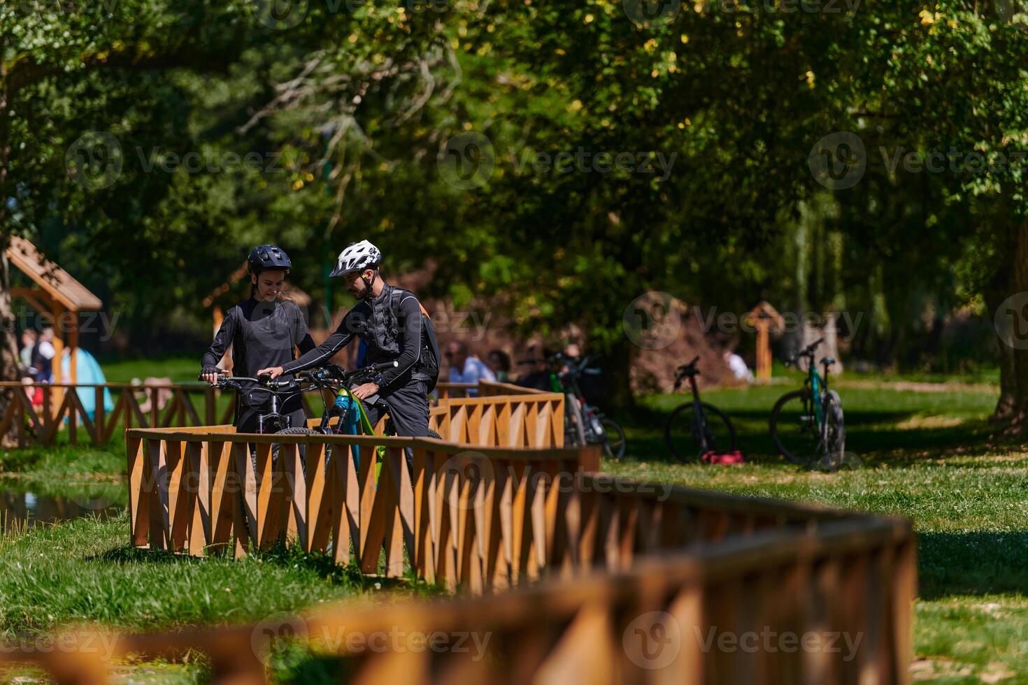 A blissful couple, adorned in professional cycling gear, enjoys a romantic bicycle ride through a park, surrounded by modern natural attractions, radiating love and happiness photo