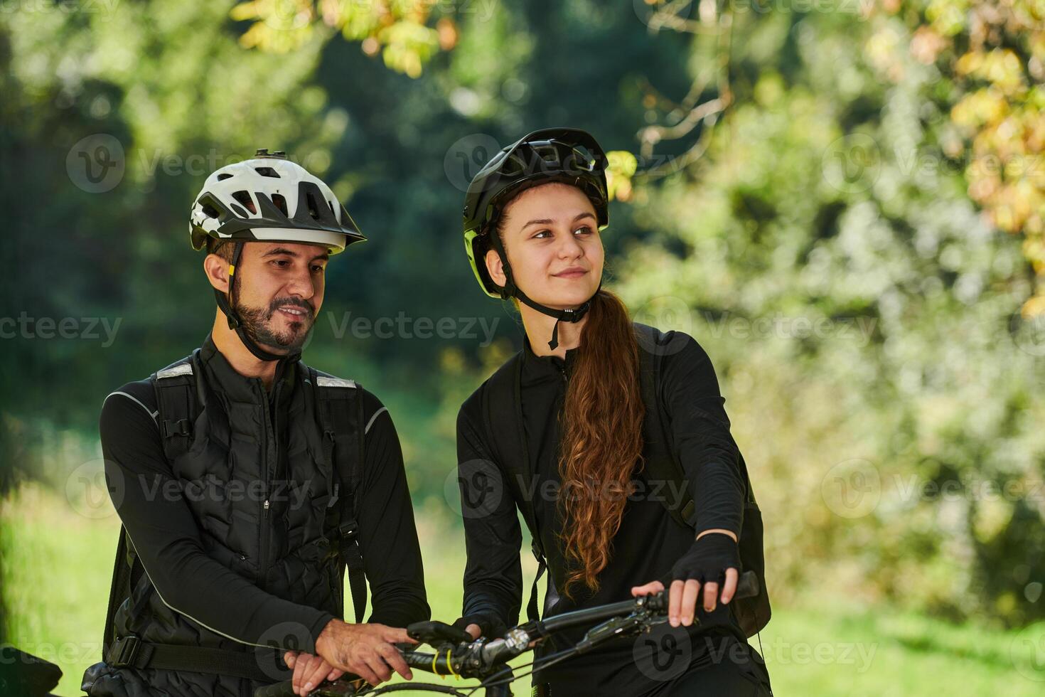 A blissful couple, adorned in professional cycling gear, enjoys a romantic bicycle ride through a park, surrounded by modern natural attractions, radiating love and happiness photo