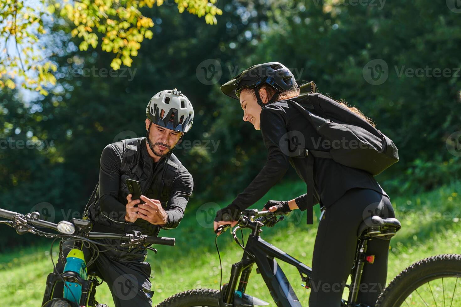 A sweet couple, equipped with bicycles and engrossed in coordinating their journey, checks their GPS mobile and watches while planning scenic routes in the park, seamlessly blending technology and photo