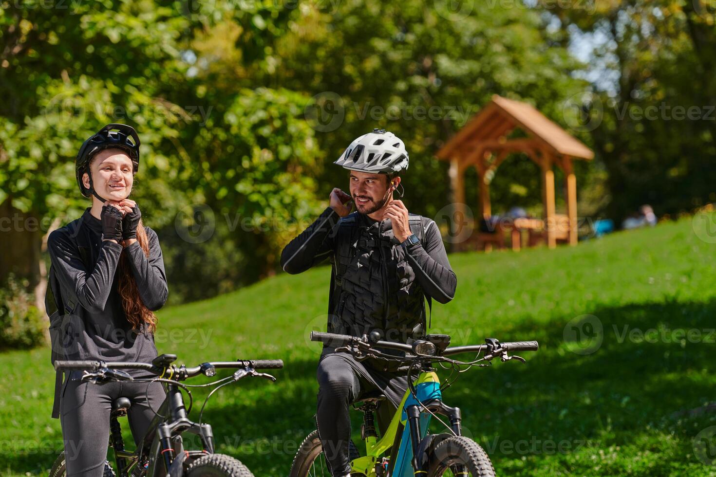 A sweet couple, equipped with bicycles and engrossed in coordinating their journey, checks their GPS mobile and watches while planning scenic routes in the park, seamlessly blending technology and photo