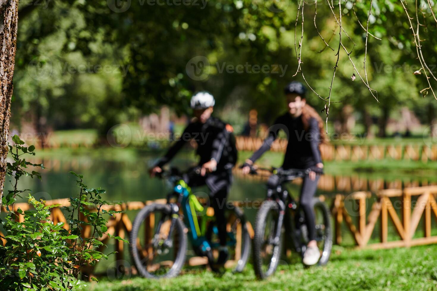 A blissful couple, adorned in professional cycling gear, enjoys a romantic bicycle ride through a park, surrounded by modern natural attractions, radiating love and happiness photo