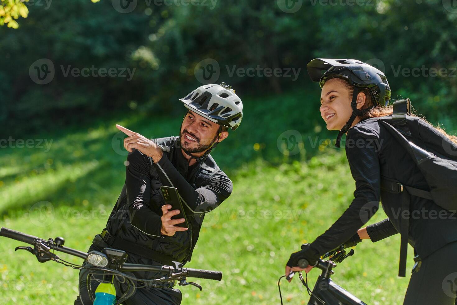 A sweet couple, equipped with bicycles and engrossed in coordinating their journey, checks their GPS mobile and watches while planning scenic routes in the park, seamlessly blending technology and photo