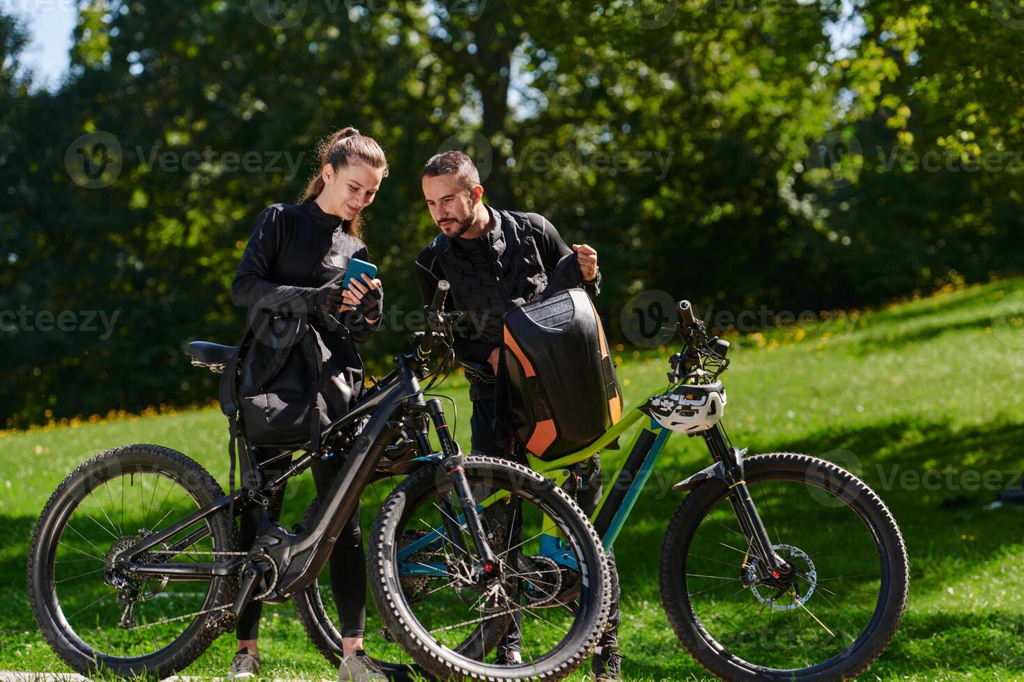 A sweet couple, equipped with bicycles and engrossed in coordinating their journey, checks their GPS mobile and watches while planning scenic routes in the park, seamlessly blending technology and photo