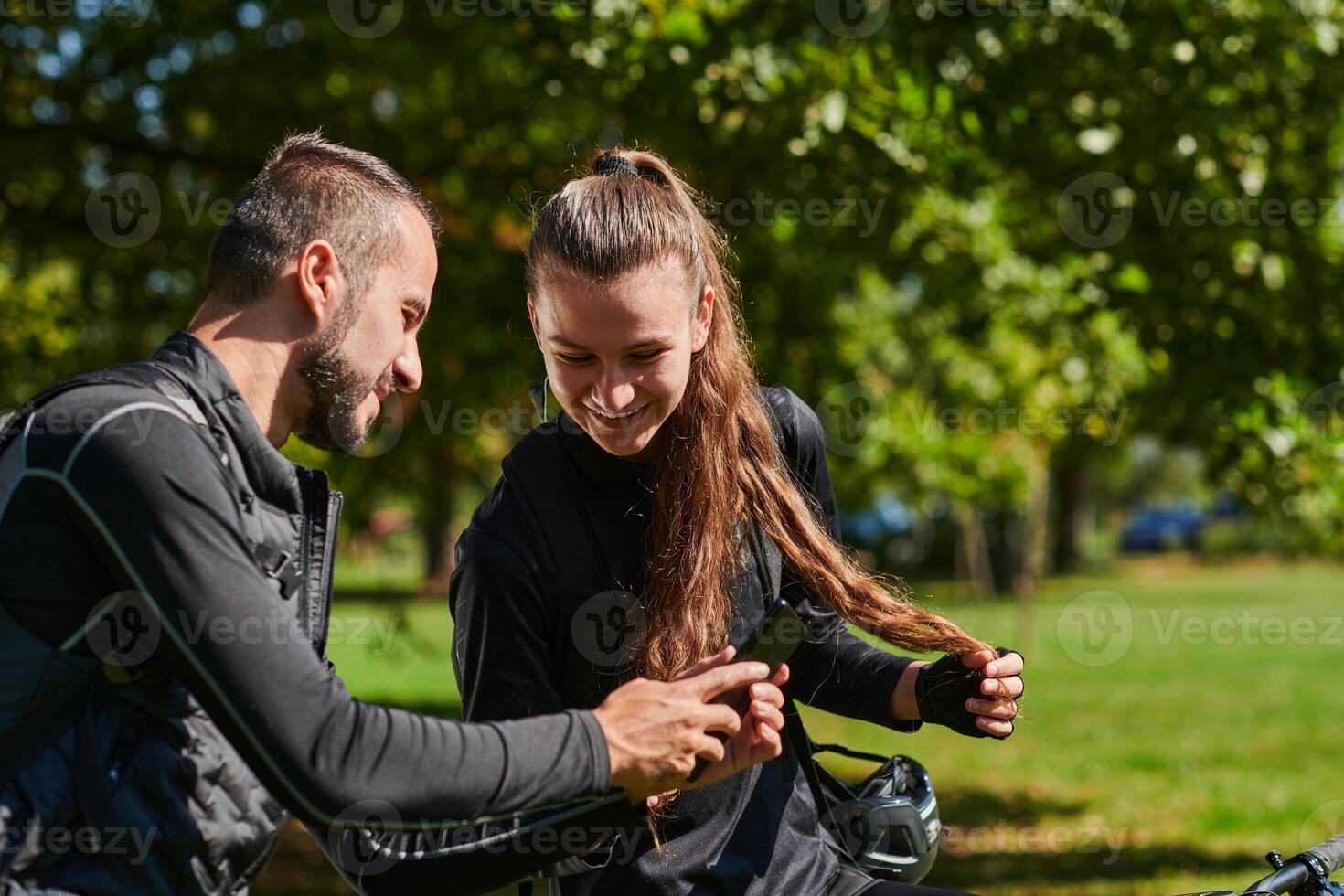 A sweet couple, equipped with bicycles and engrossed in coordinating their journey, checks their GPS mobile and watches while planning scenic routes in the park, seamlessly blending technology and photo