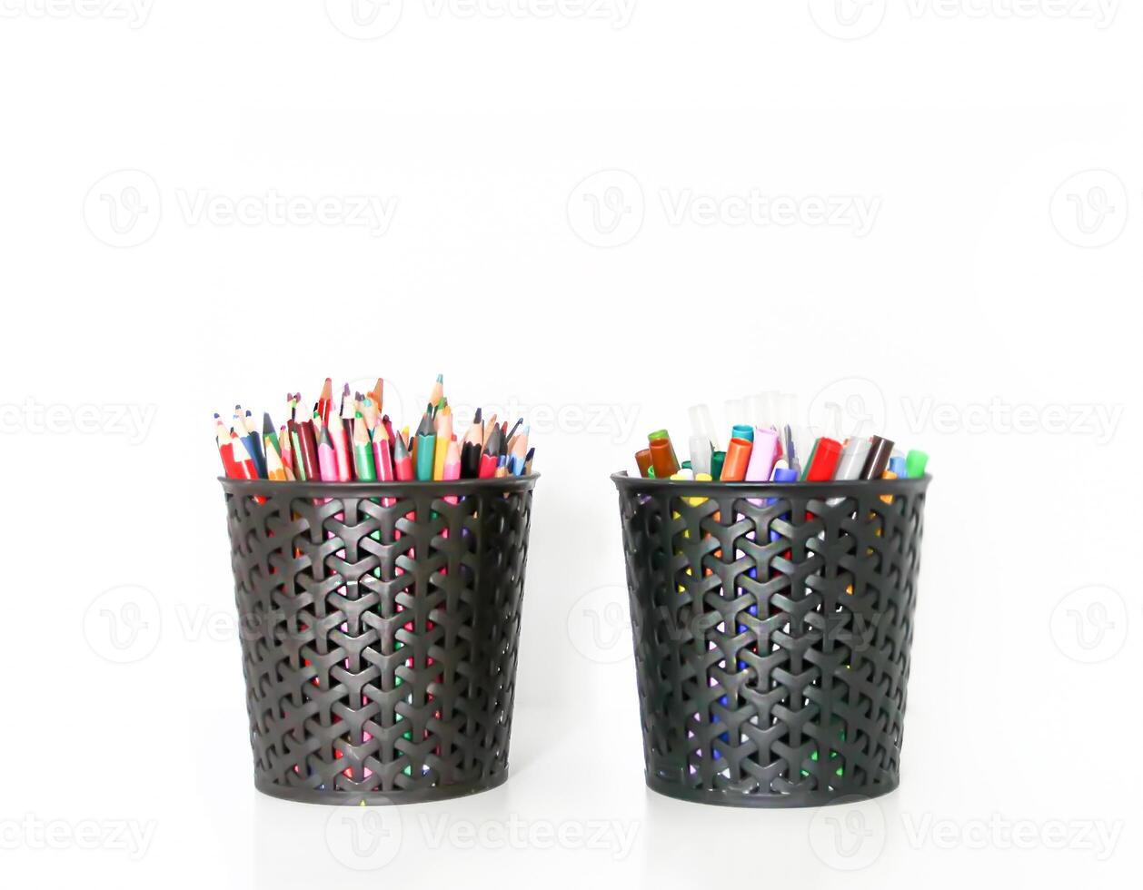 Colored crayons, pencils and pens in black containers on a white shelf. photo