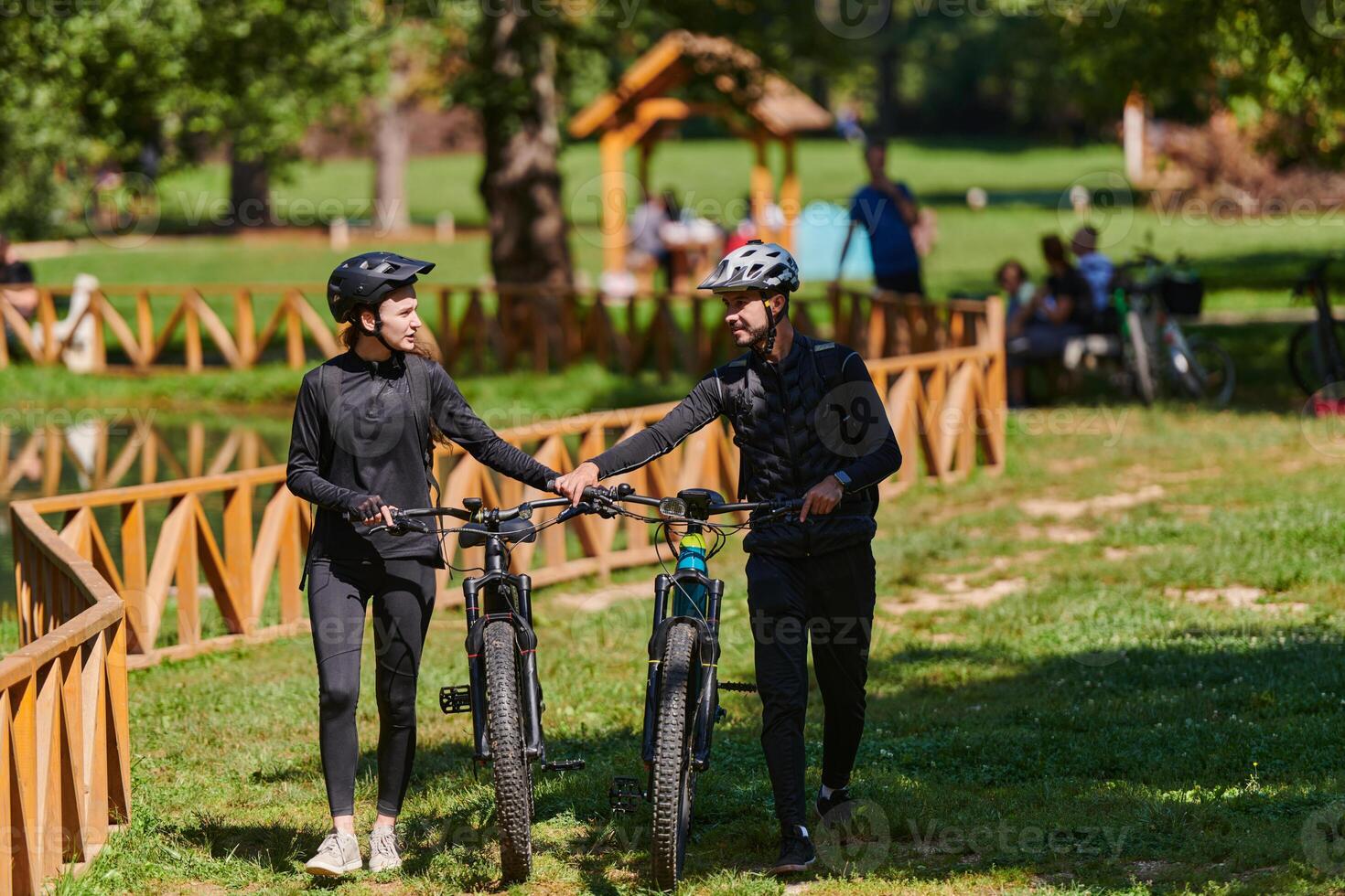A sweet couple, equipped with bicycles and engrossed in coordinating their journey, checks their GPS mobile and watches while planning scenic routes in the park, seamlessly blending technology and photo