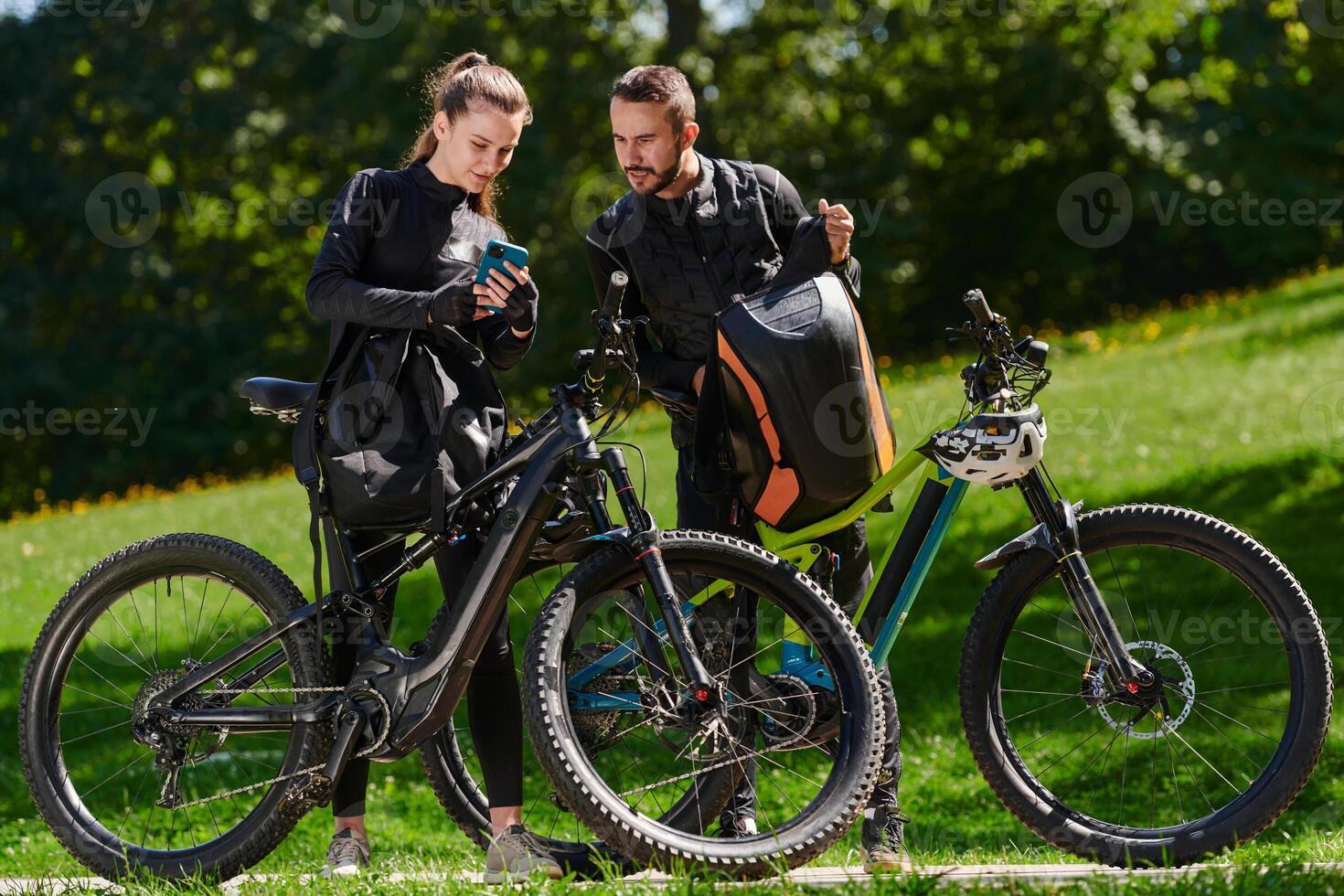 A sweet couple, equipped with bicycles and engrossed in coordinating their journey, checks their GPS mobile and watches while planning scenic routes in the park, seamlessly blending technology and photo