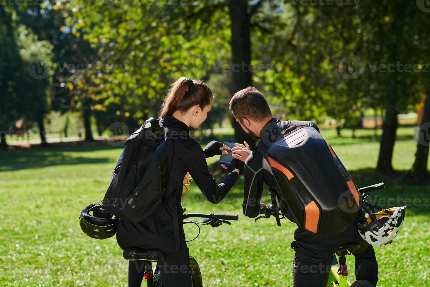 A sweet couple, equipped with bicycles and engrossed in coordinating their journey, checks their GPS mobile and watches while planning scenic routes in the park, seamlessly blending technology and photo