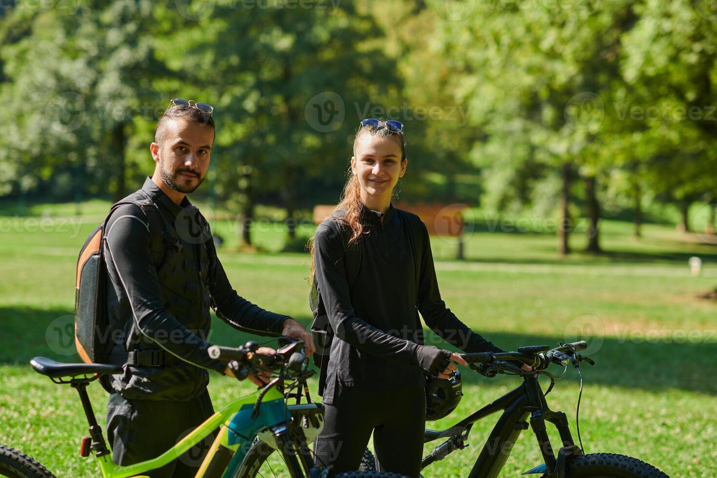 A blissful couple, adorned in professional cycling gear, enjoys a romantic bicycle ride through a park, surrounded by modern natural attractions, radiating love and happiness photo