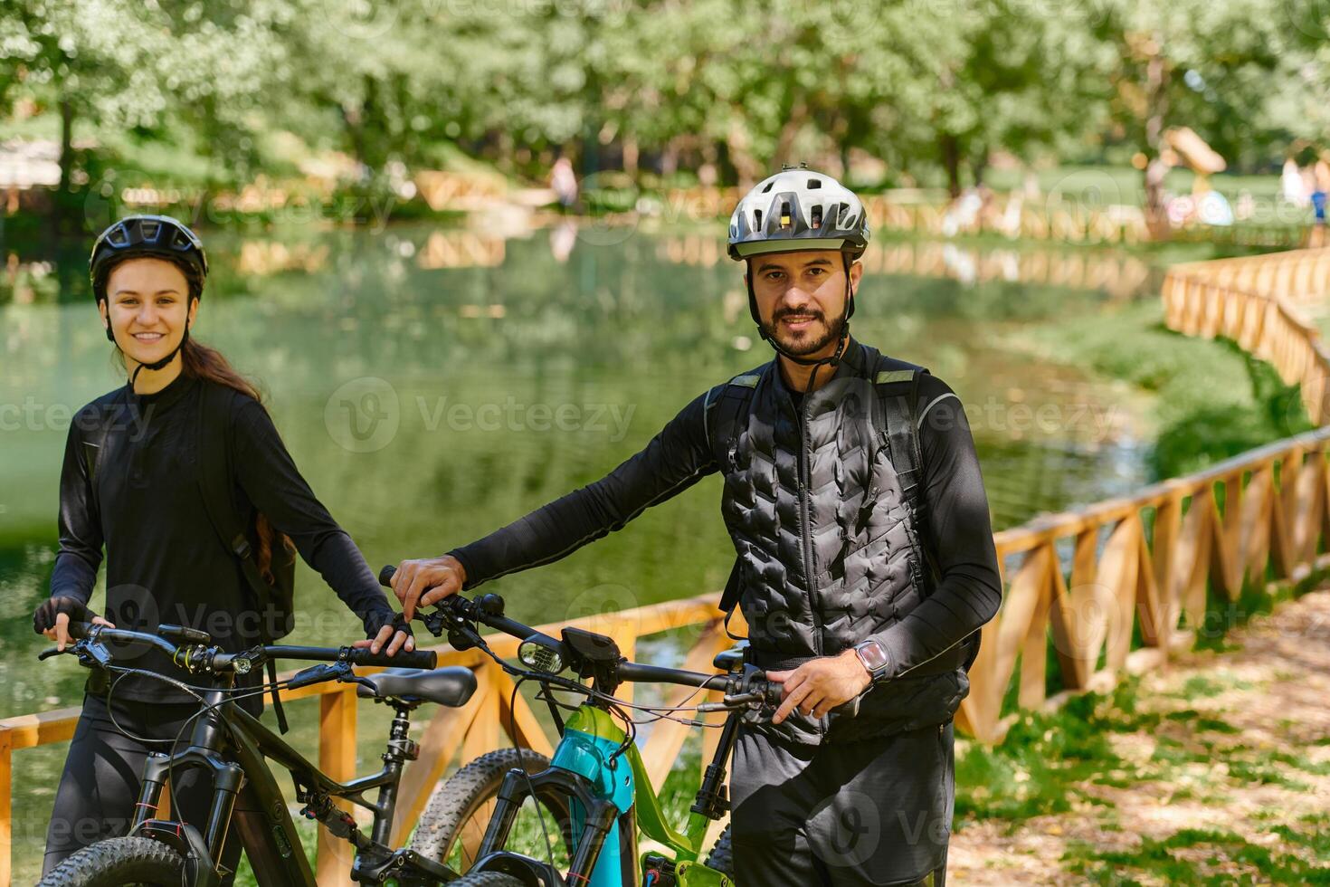 A blissful couple, adorned in professional cycling gear, enjoys a romantic bicycle ride through a park, surrounded by modern natural attractions, radiating love and happiness photo