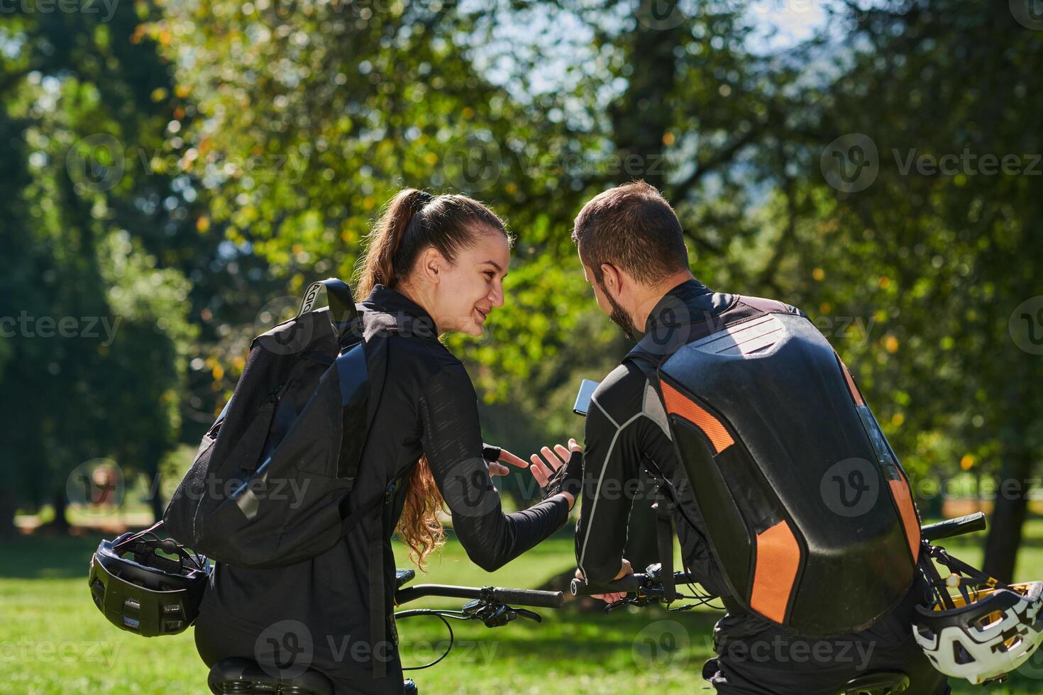 A sweet couple, equipped with bicycles and engrossed in coordinating their journey, checks their GPS mobile and watches while planning scenic routes in the park, seamlessly blending technology and photo