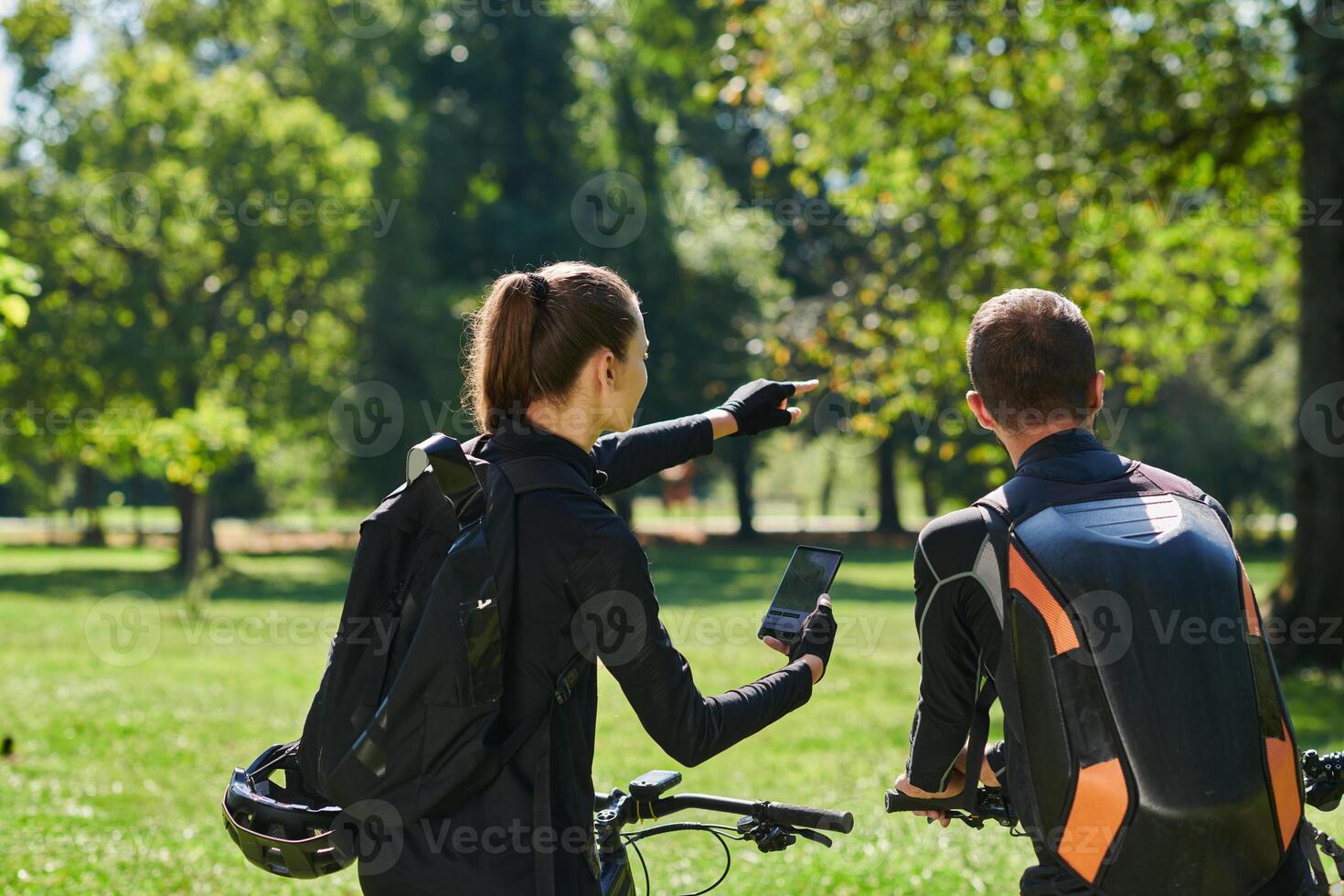 A sweet couple, equipped with bicycles and engrossed in coordinating their journey, checks their GPS mobile and watches while planning scenic routes in the park, seamlessly blending technology and photo
