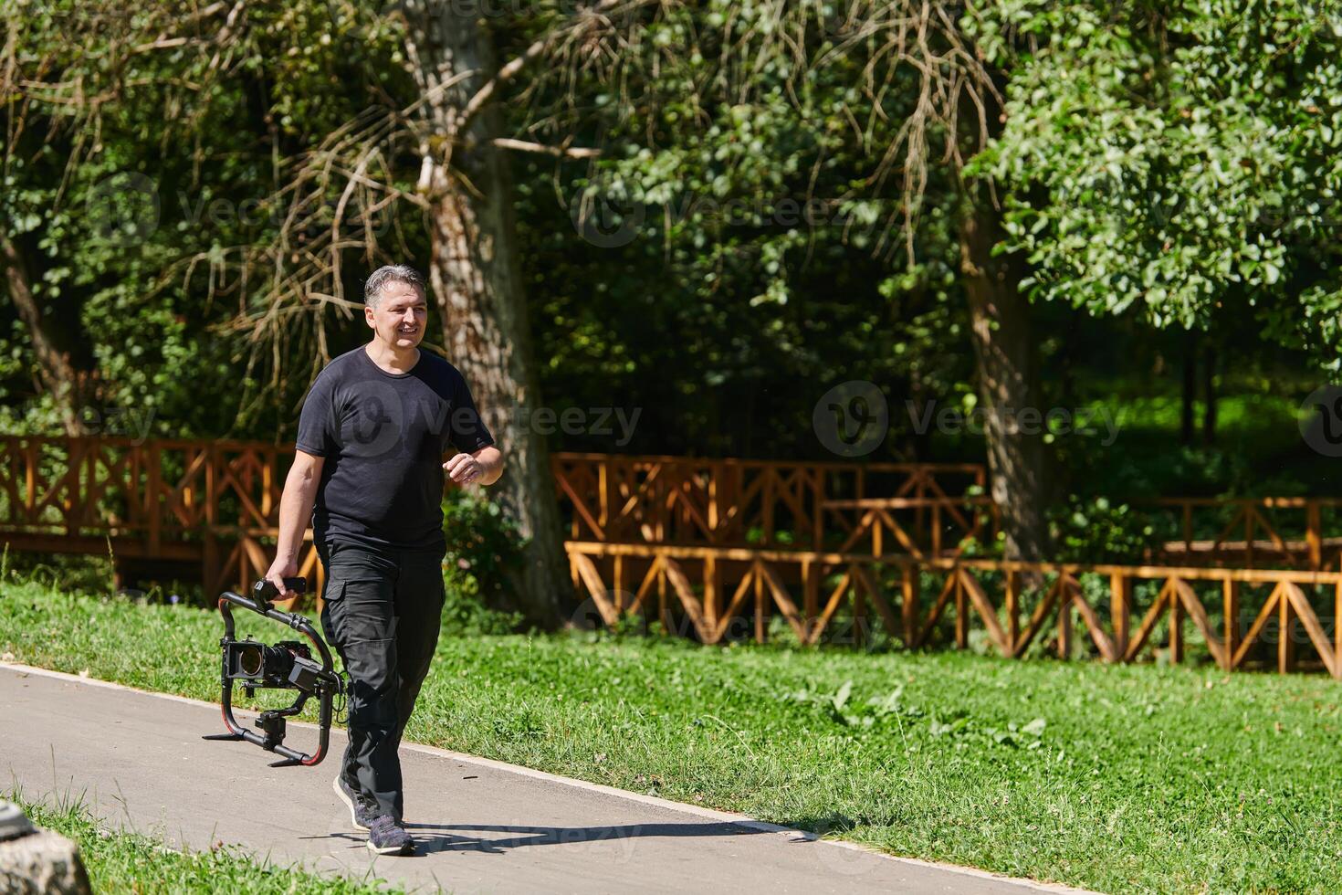 After completing a cinematic venture, a skilled videographer, adorned with camera equipment, leisurely strolls through the park, capturing the essence of post-production satisfaction and creative photo