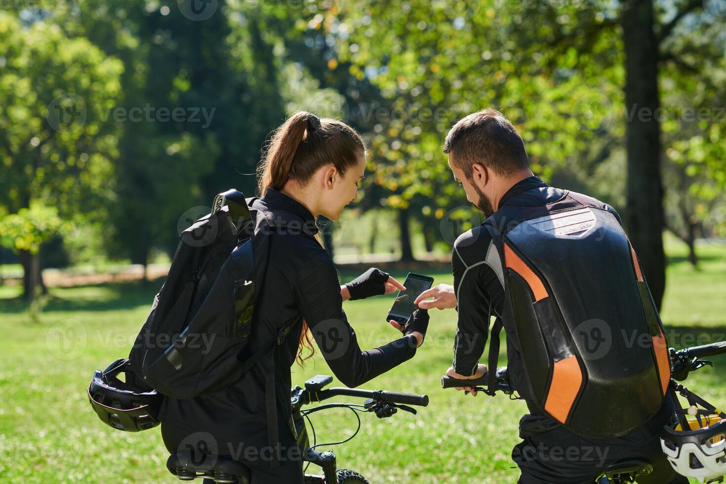 A sweet couple, equipped with bicycles and engrossed in coordinating their journey, checks their GPS mobile and watches while planning scenic routes in the park, seamlessly blending technology and photo