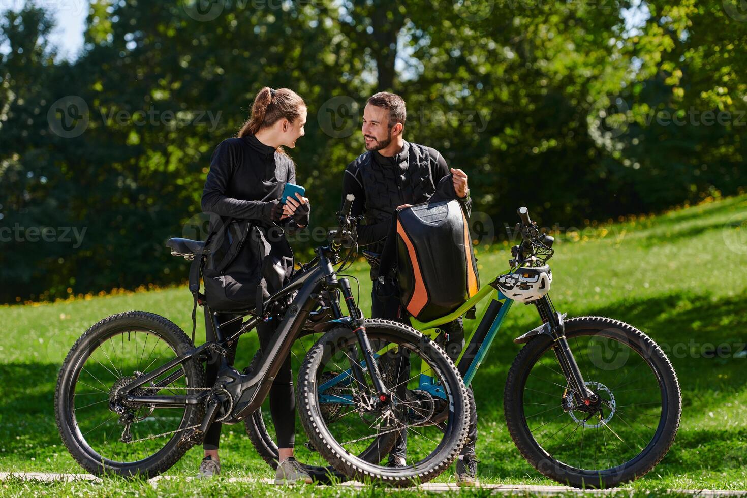 A sweet couple, equipped with bicycles and engrossed in coordinating their journey, checks their GPS mobile and watches while planning scenic routes in the park, seamlessly blending technology and photo