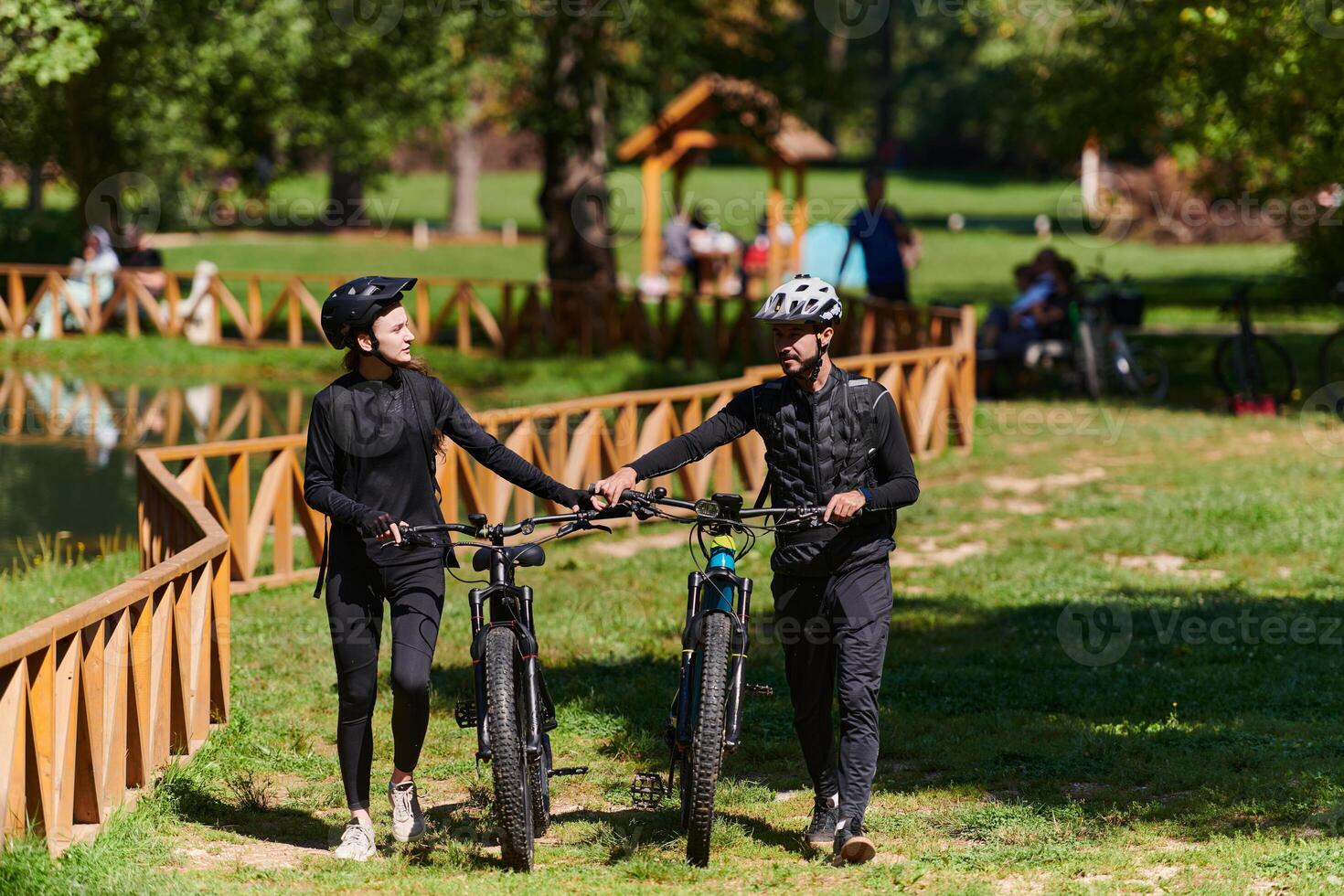 A blissful couple, adorned in professional cycling gear, enjoys a romantic bicycle ride through a park, surrounded by modern natural attractions, radiating love and happiness photo