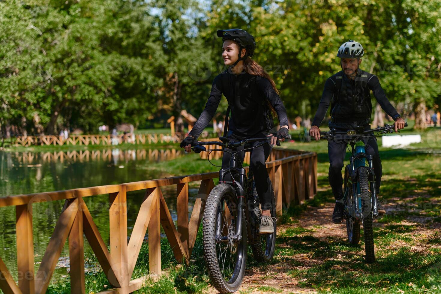 A blissful couple, adorned in professional cycling gear, enjoys a romantic bicycle ride through a park, surrounded by modern natural attractions, radiating love and happiness photo