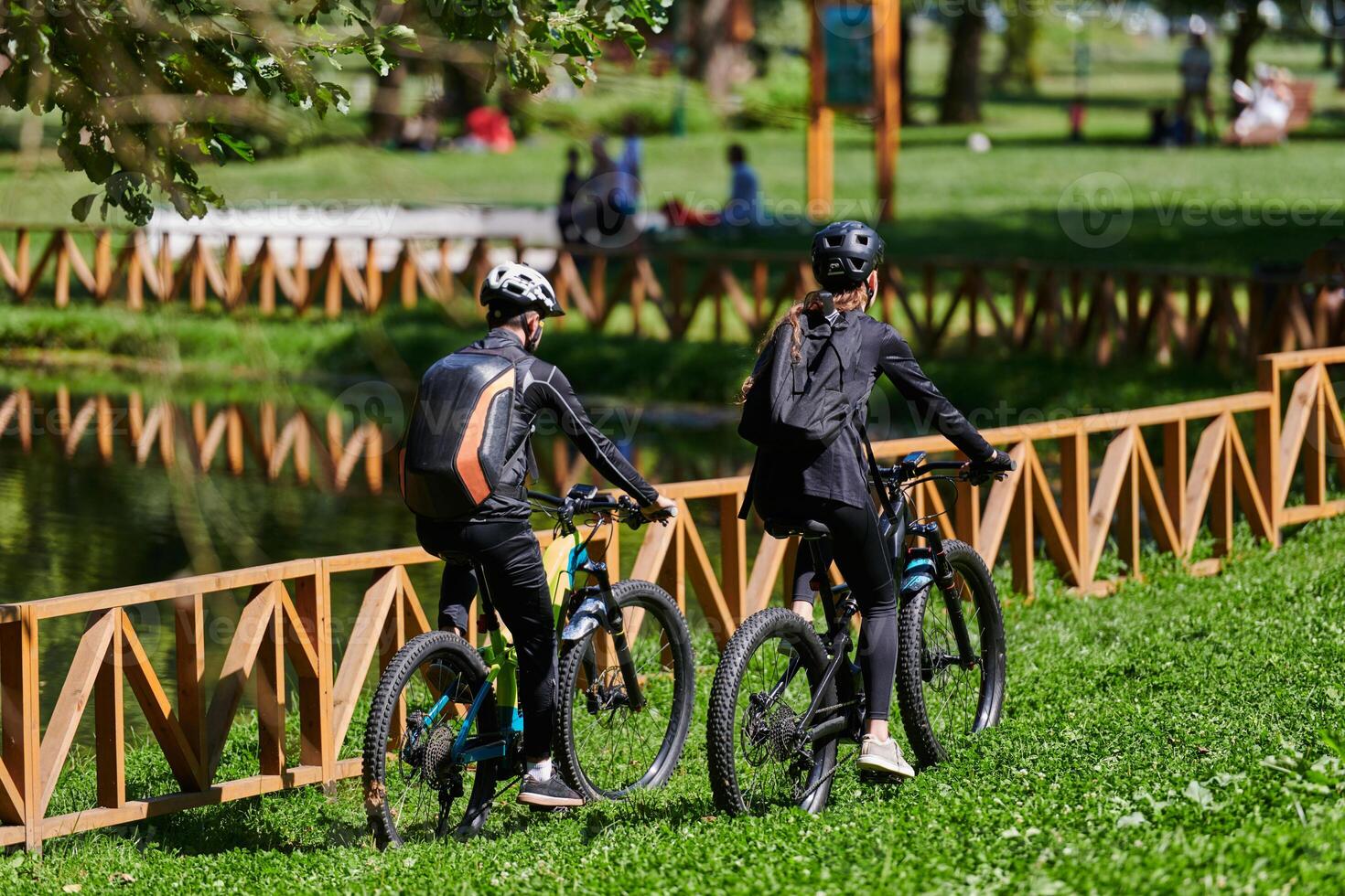 A blissful couple, adorned in professional cycling gear, enjoys a romantic bicycle ride through a park, surrounded by modern natural attractions, radiating love and happiness photo