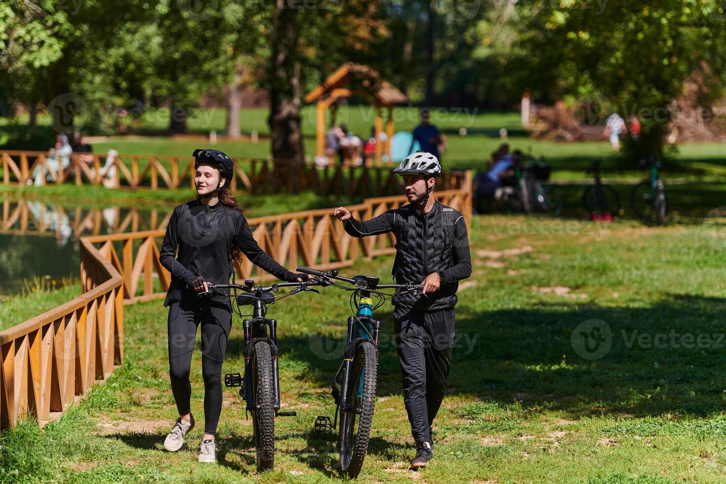 A blissful couple, adorned in professional cycling gear, enjoys a romantic bicycle ride through a park, surrounded by modern natural attractions, radiating love and happiness photo