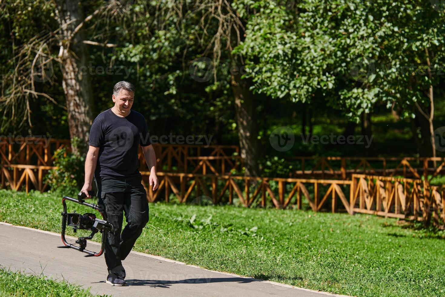 After completing a cinematic venture, a skilled videographer, adorned with camera equipment, leisurely strolls through the park, capturing the essence of post-production satisfaction and creative photo
