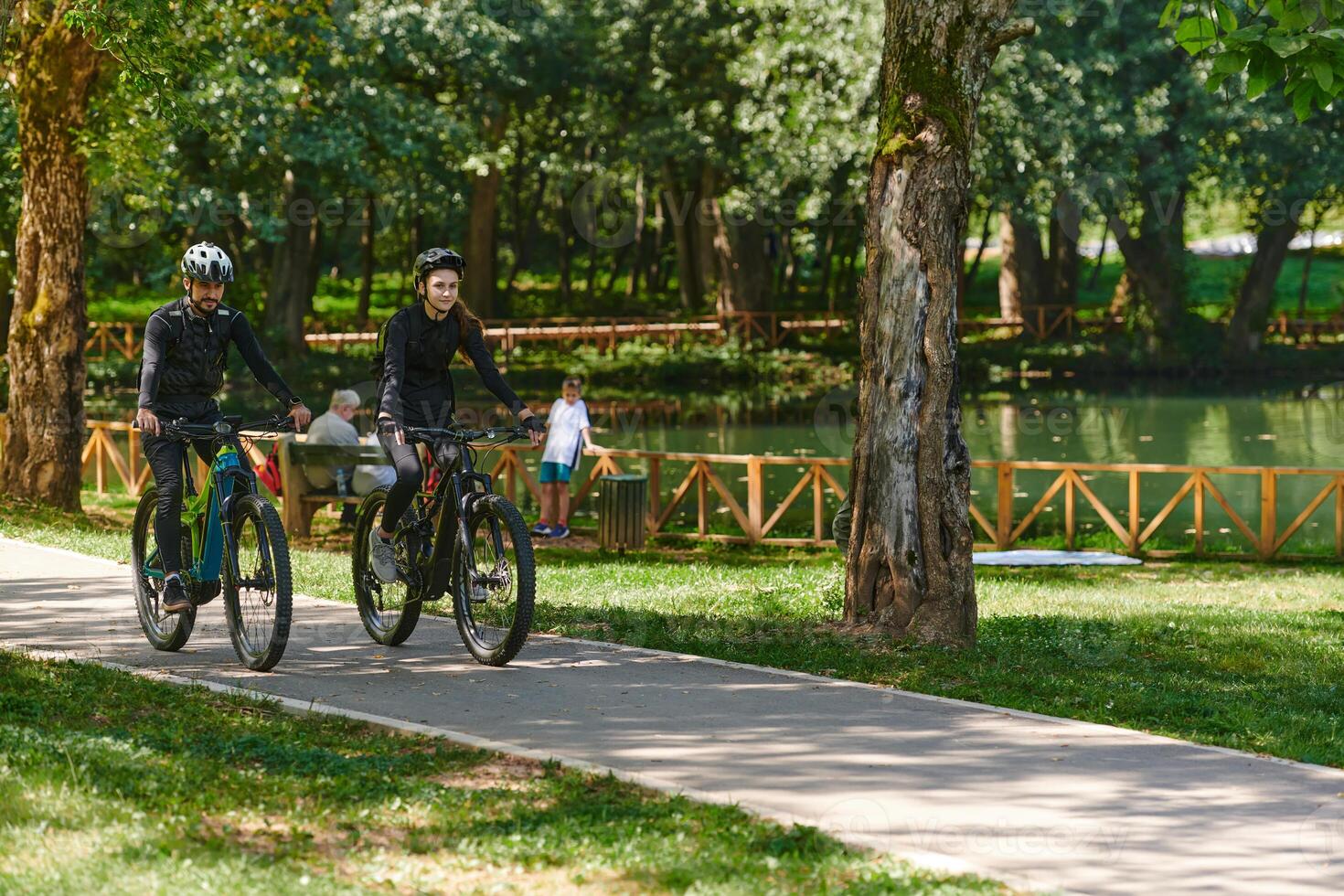A blissful couple, adorned in professional cycling gear, enjoys a romantic bicycle ride through a park, surrounded by modern natural attractions, radiating love and happiness photo