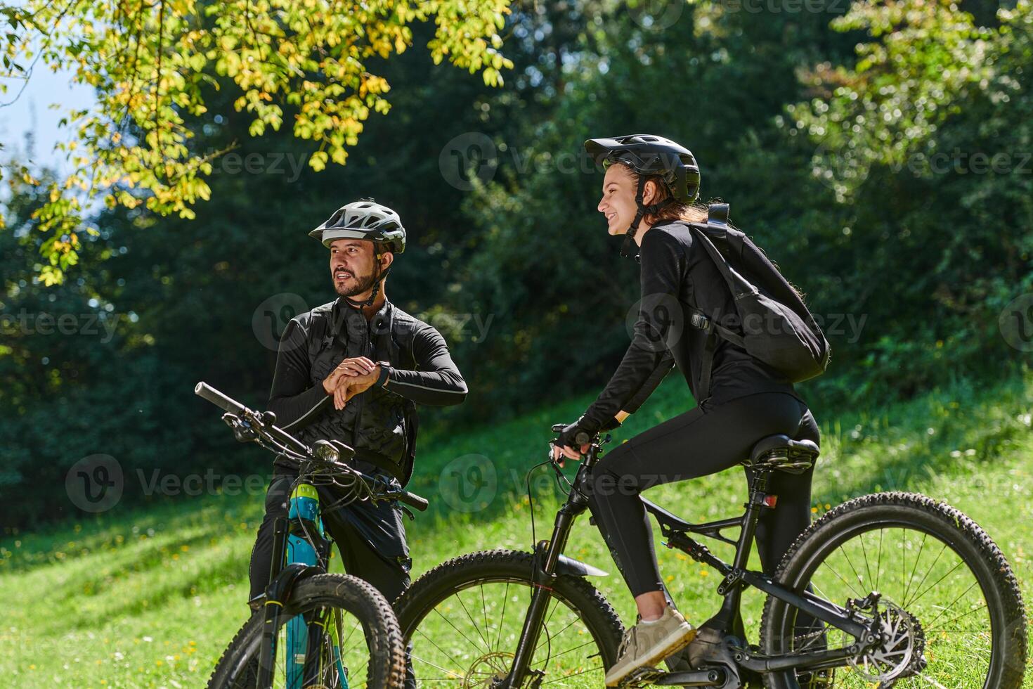 A sweet couple, equipped with bicycles and engrossed in coordinating their journey, checks their GPS mobile and watches while planning scenic routes in the park, seamlessly blending technology and photo