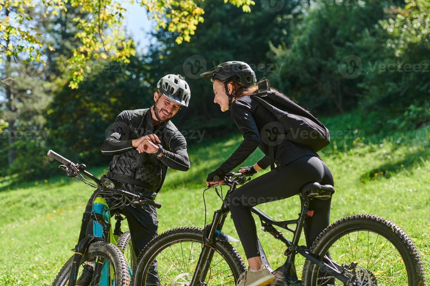 A sweet couple, equipped with bicycles and engrossed in coordinating their journey, checks their GPS mobile and watches while planning scenic routes in the park, seamlessly blending technology and photo