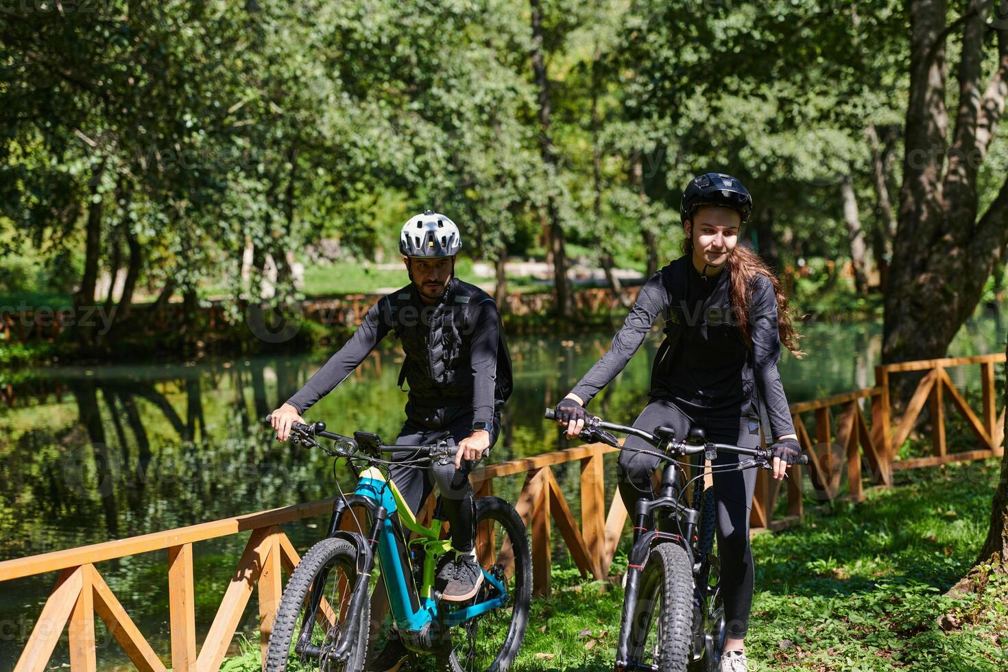 A blissful couple, adorned in professional cycling gear, enjoys a romantic bicycle ride through a park, surrounded by modern natural attractions, radiating love and happiness photo