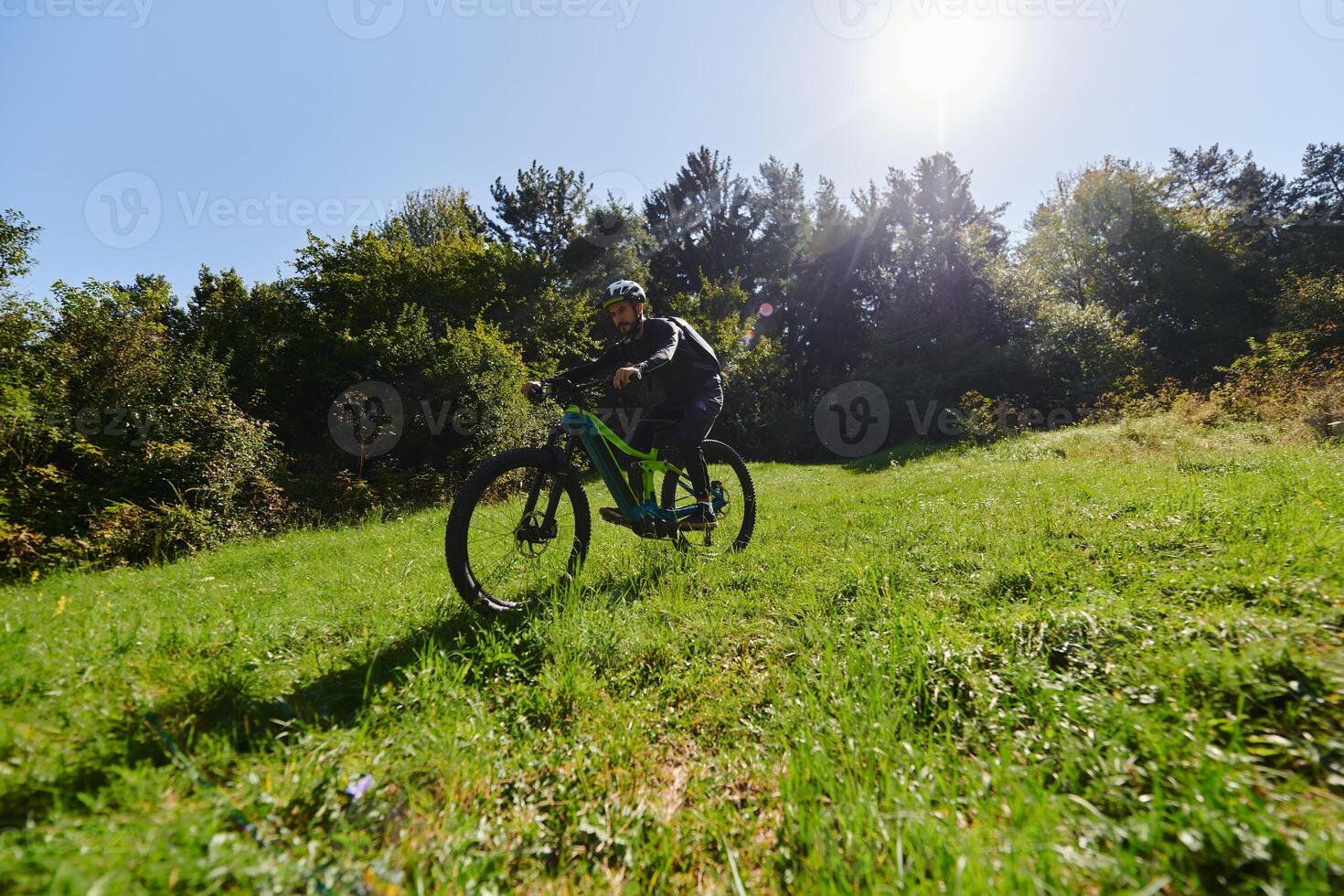 In the radiant glow of a sunny day, a fitness enthusiast, donned in professional gear, pedals through the park on his bicycle, embodying strength and vitality in a dynamic outdoor workout photo