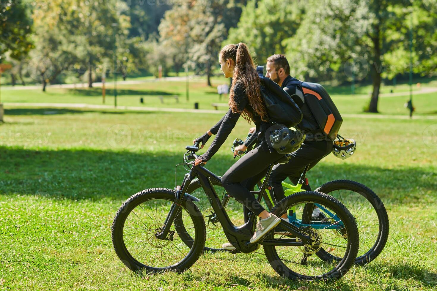 A blissful couple, adorned in professional cycling gear, enjoys a romantic bicycle ride through a park, surrounded by modern natural attractions, radiating love and happiness photo